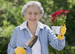 Lächelnde Dame im Garten mit Blumentopf und Schaufel in der Hand